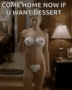 a naked woman in a bikini with whipped cream on her chest is standing in a room .