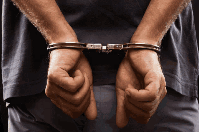 a man with his hands behind his back in handcuffs has a gray shirt on