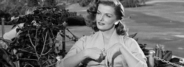 a black and white photo of a woman sitting on a bench in a park .