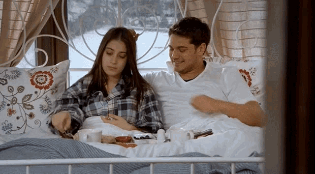 a man and a woman are laying in bed with a plate of food