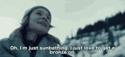 a woman is standing in the snow and smiling while talking about sunbathing and getting a bronze on .