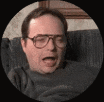 a man wearing glasses is sitting on a couch and yawning