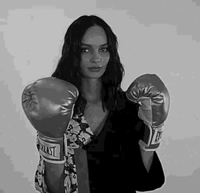 a woman wearing boxing gloves is standing in front of a white wall .