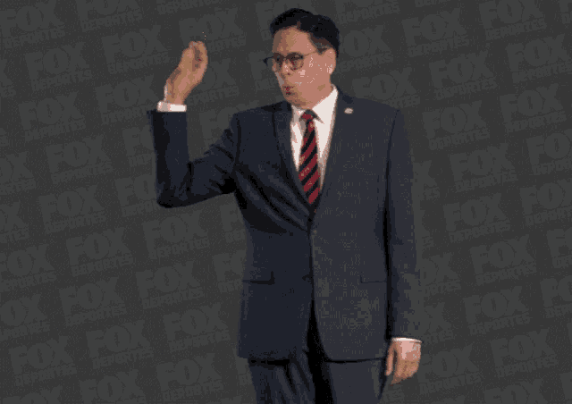 a man in a suit and tie is standing in front of a fox logo