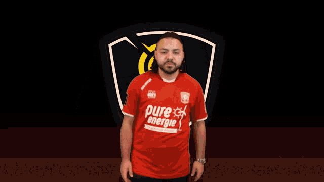 a man in a red pure energie shirt points upwards