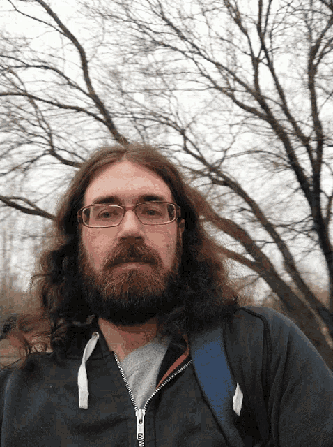 a man with long hair and glasses is wearing a black jacket