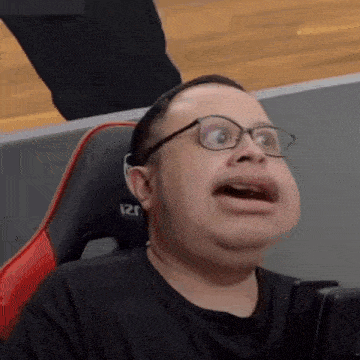 a man wearing glasses and a black shirt is making a funny face while sitting in a chair .