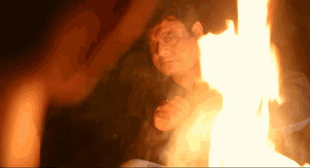 a man is sitting in front of a fire with smoke coming out of it