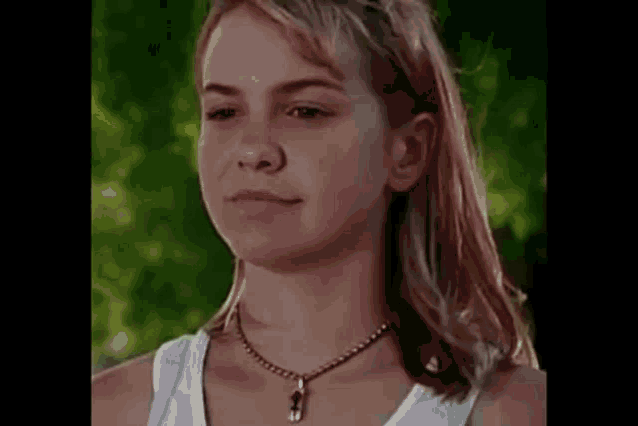a young girl wearing a necklace and a white tank top is making a funny face .