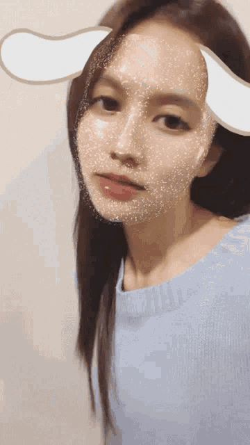a woman wearing a blue sweater has a bunny ear sticker on her face