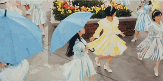 a group of girls in dresses are dancing with umbrellas .