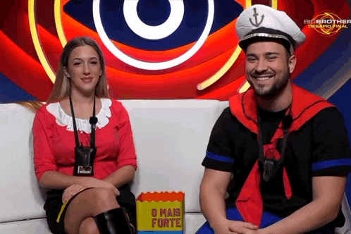 a man and a woman are sitting on a couch in front of a big brother sign