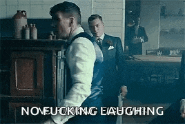 a man in a suit and tie is holding a sword while another man stands behind him .