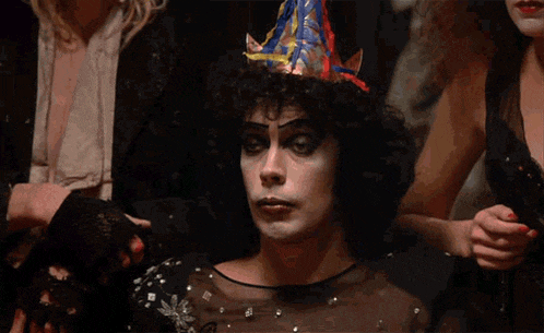a man with a party hat on his head is sitting with his hands folded .