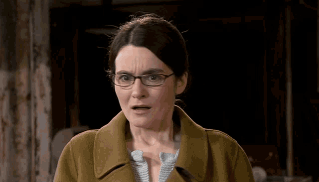a woman wearing glasses and a brown coat making a funny face