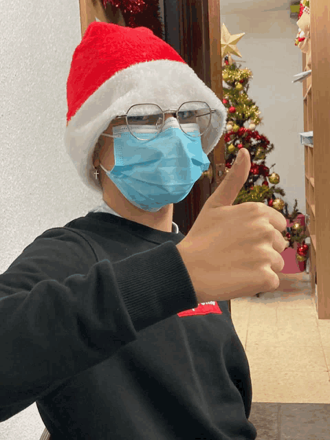 a person wearing a santa hat and face mask giving a thumbs up