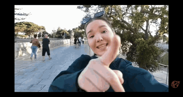 a woman is giving a thumbs up in front of a tree