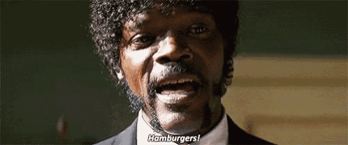 a man with curly hair and a beard is wearing a suit and tie and talking about hamburgers .