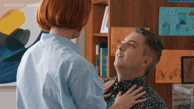 a woman is touching a man 's neck in front of a workin moms poster