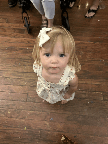 a little girl with a white bow in her hair is standing on a wooden floor
