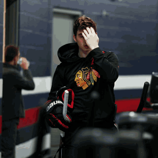 a hockey player wearing a blackhawks sweatshirt covers his face with his hand