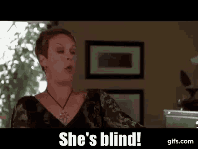 a woman is sitting at a table in a living room talking to someone and says `` she 's blind ! ''