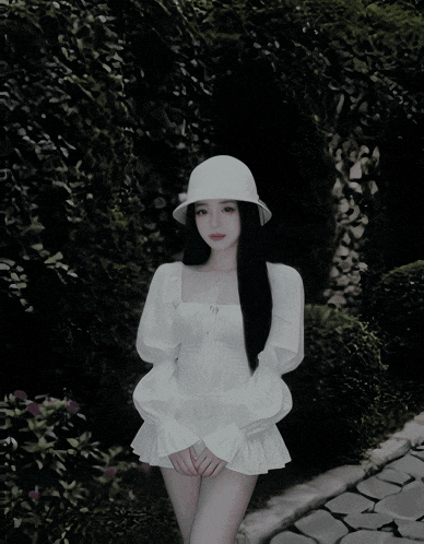 a woman wearing a white hat and a white dress is standing on a path