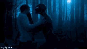 a man and a woman are kissing in the dark in front of trees .