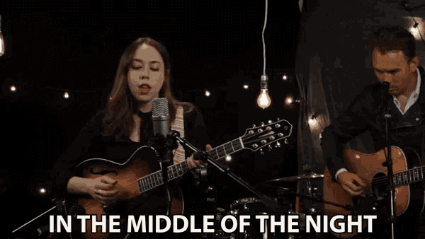 a woman sings into a microphone while a man plays a guitar and the words in the middle of the night are visible