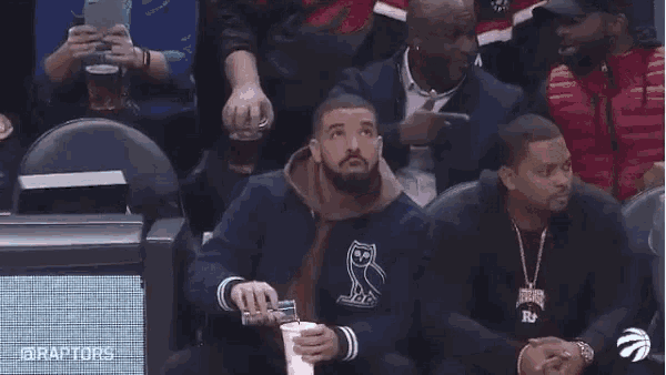 a man is sitting in the stands of a basketball game holding a cup of coffee .