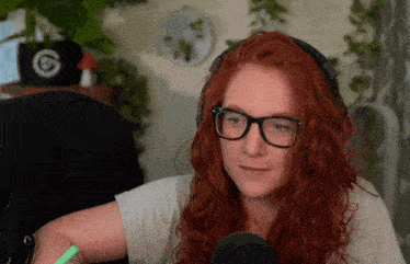 a woman with red hair wearing glasses and headphones has a green marker in her hand