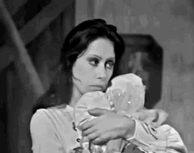 a black and white photo of a woman holding a baby doll .