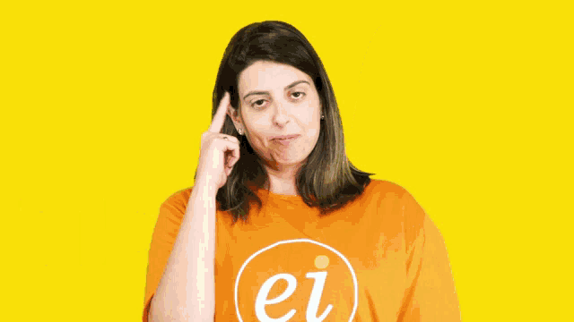 a woman wearing an orange shirt that says ei is pointing at something