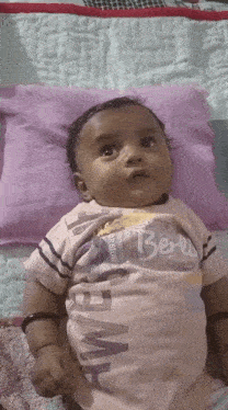 a baby wearing a shirt that says berry is laying on a purple pillow