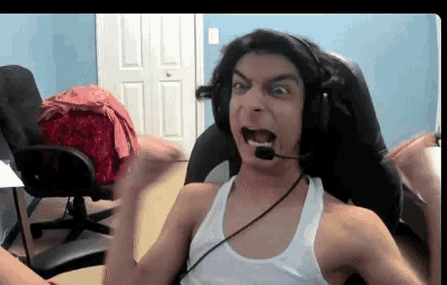 a man wearing headphones and a white tank top is making a funny face while sitting in a chair .