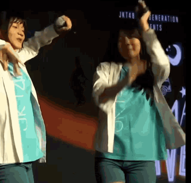 two girls are dancing in front of a sign that says jkt48 generation ent