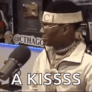 a man wearing a headband and glasses is sitting in front of a microphone and saying `` a kissss '' .