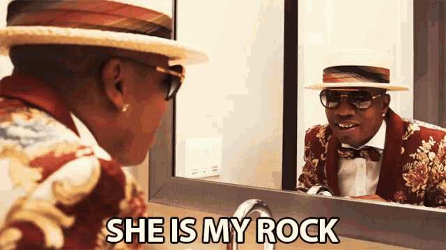 a man in a hat is looking at his reflection in a mirror and the words she is my rock are above him