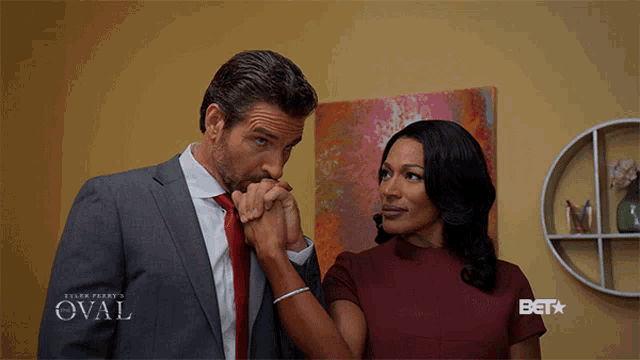 a man in a suit and tie kisses a woman 's hand with oval written on the bottom