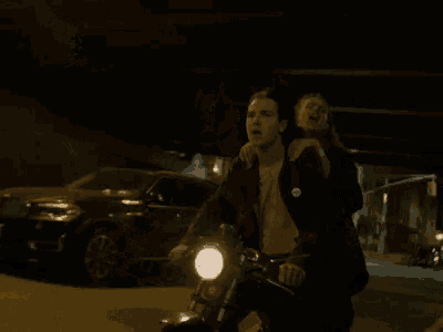 a man and a woman are riding a motorcycle down a street at night .