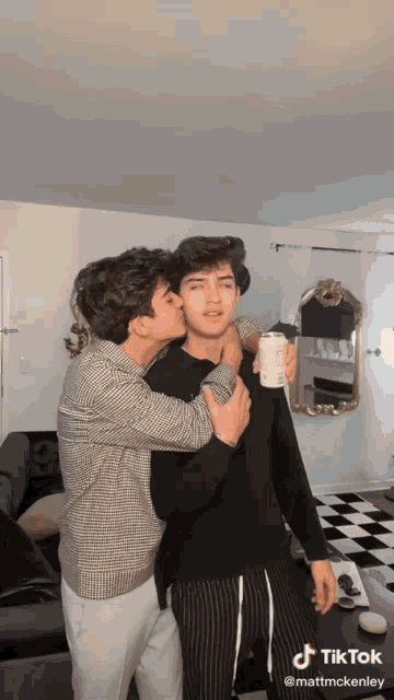 a man is kissing another man on the cheek while holding a coffee cup .