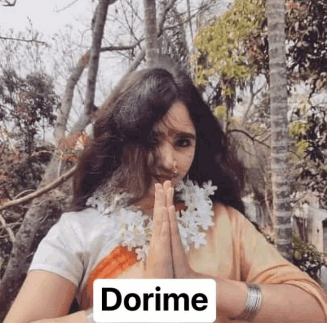 a woman wearing a sari and a nose ring is holding her hands together in a prayer position .