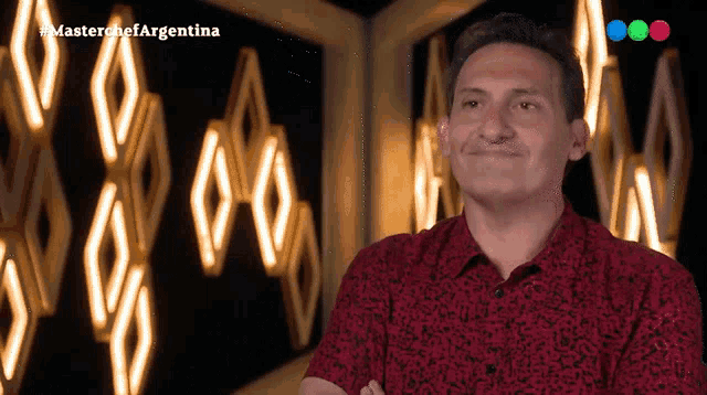 a man in a red shirt is standing in front of a wall that says master chef argentina on it