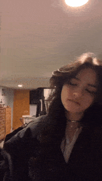 a woman with long dark hair is standing in a room with her eyes closed .