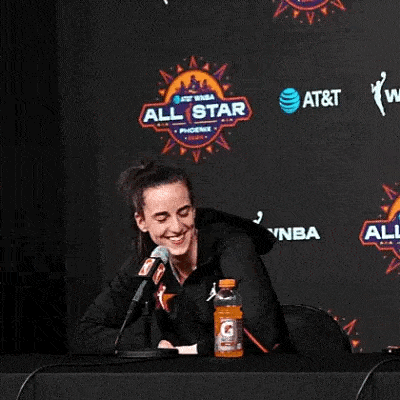 a woman is sitting at a table in front of a microphone and a bottle of gatorade .