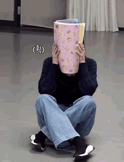 a woman sits on the floor covering her face with a pink book that says ' korean ' on it