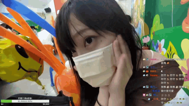 a woman wearing a face mask looks at the camera with balloons in the background and a loading bar that says 50