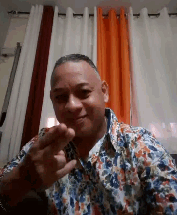 a man wearing a floral shirt points at the camera