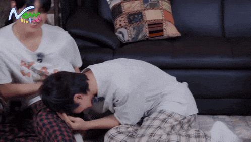 two men are sitting on the floor in front of a couch with the word now on the bottom