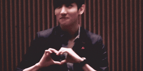 a man in a suit is making a heart with his hands